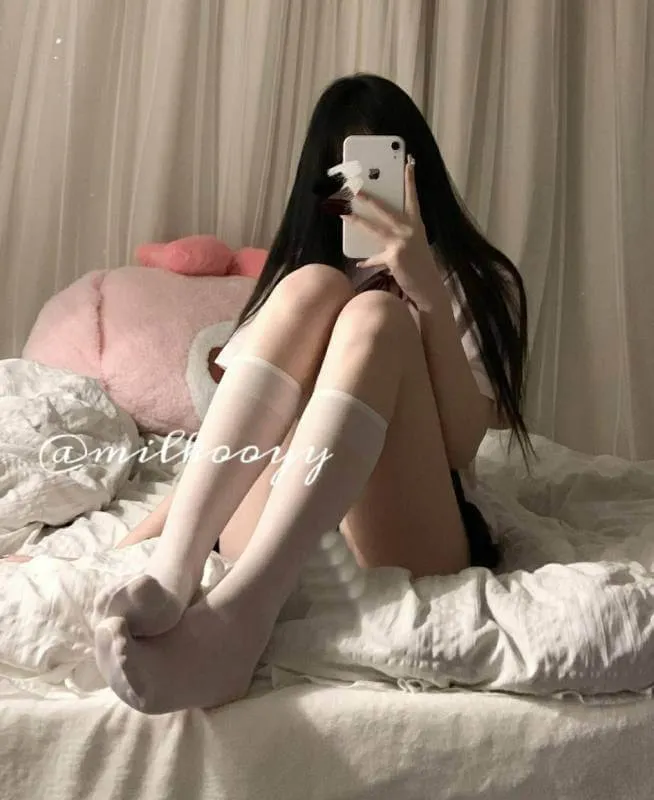 ｜抖音创作者公开 长黑发人物坐在床上，以手机遮住面部，搭配浅色长袜和深色服装