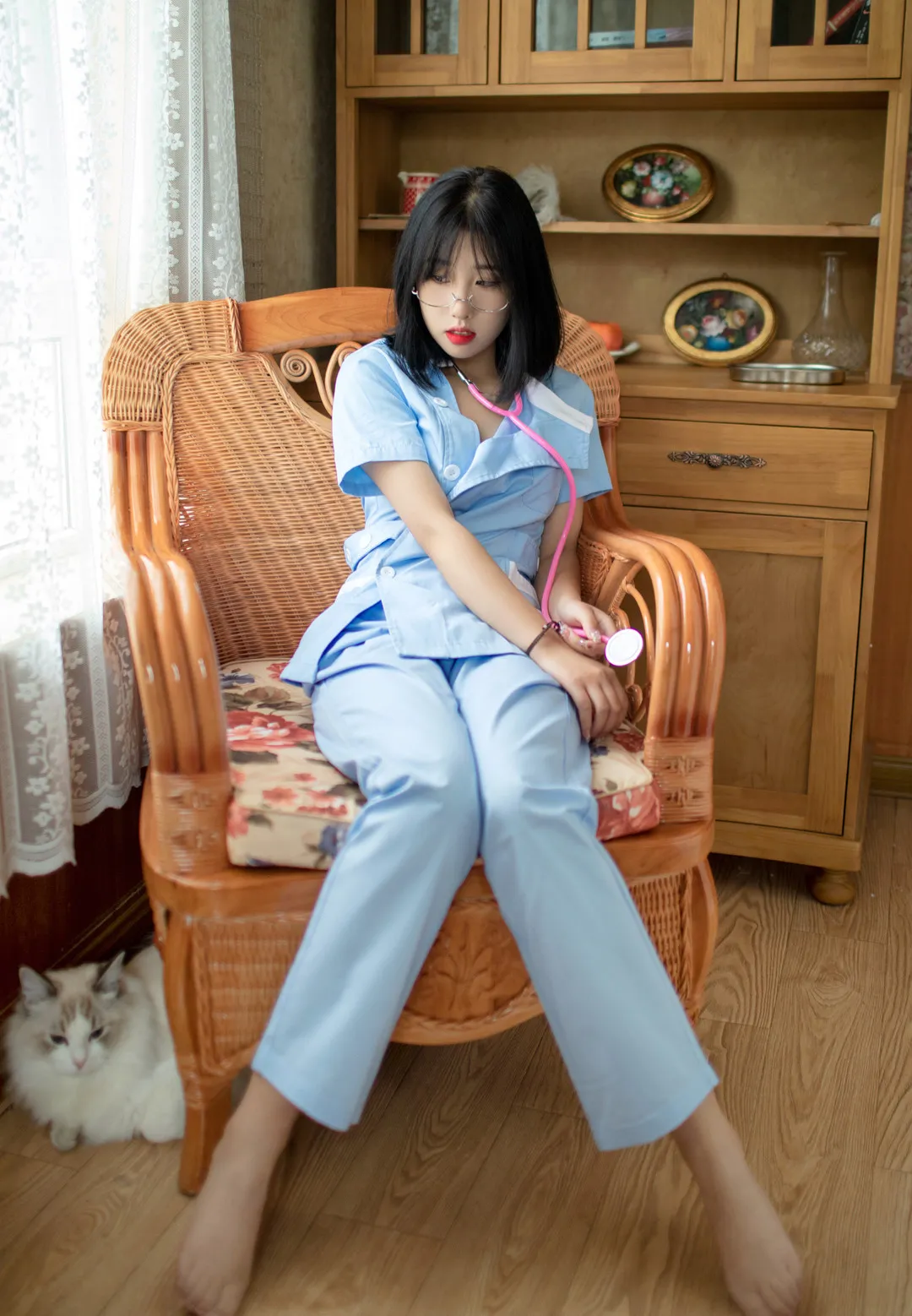 短发女生穿浅蓝色制服坐在藤椅上,佩戴眼镜并拿着粉色听诊器
