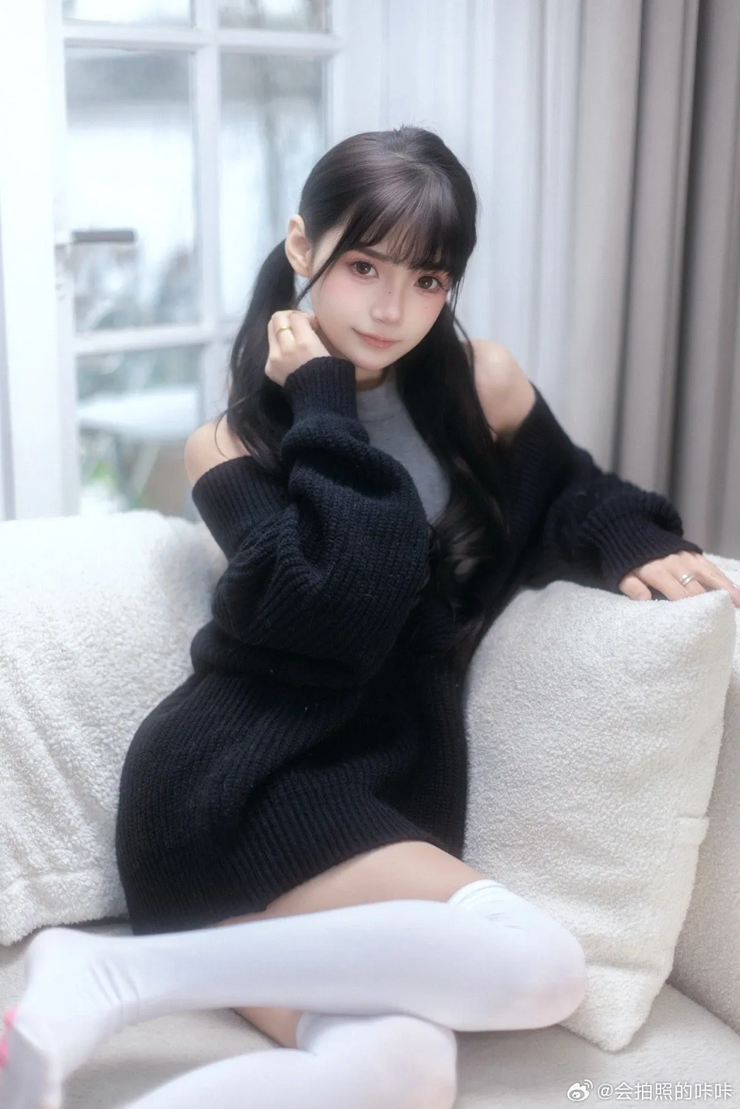 长发女生穿黑色针织外套和灰色上衣坐在白色沙发上,搭配白色长袜