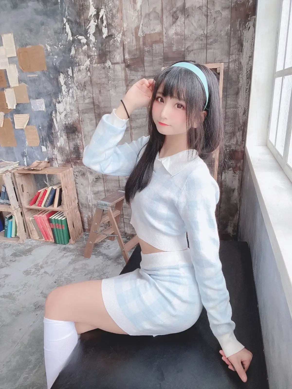 模特头戴浅蓝发箍身穿格纹针织短裙坐于黑色台面