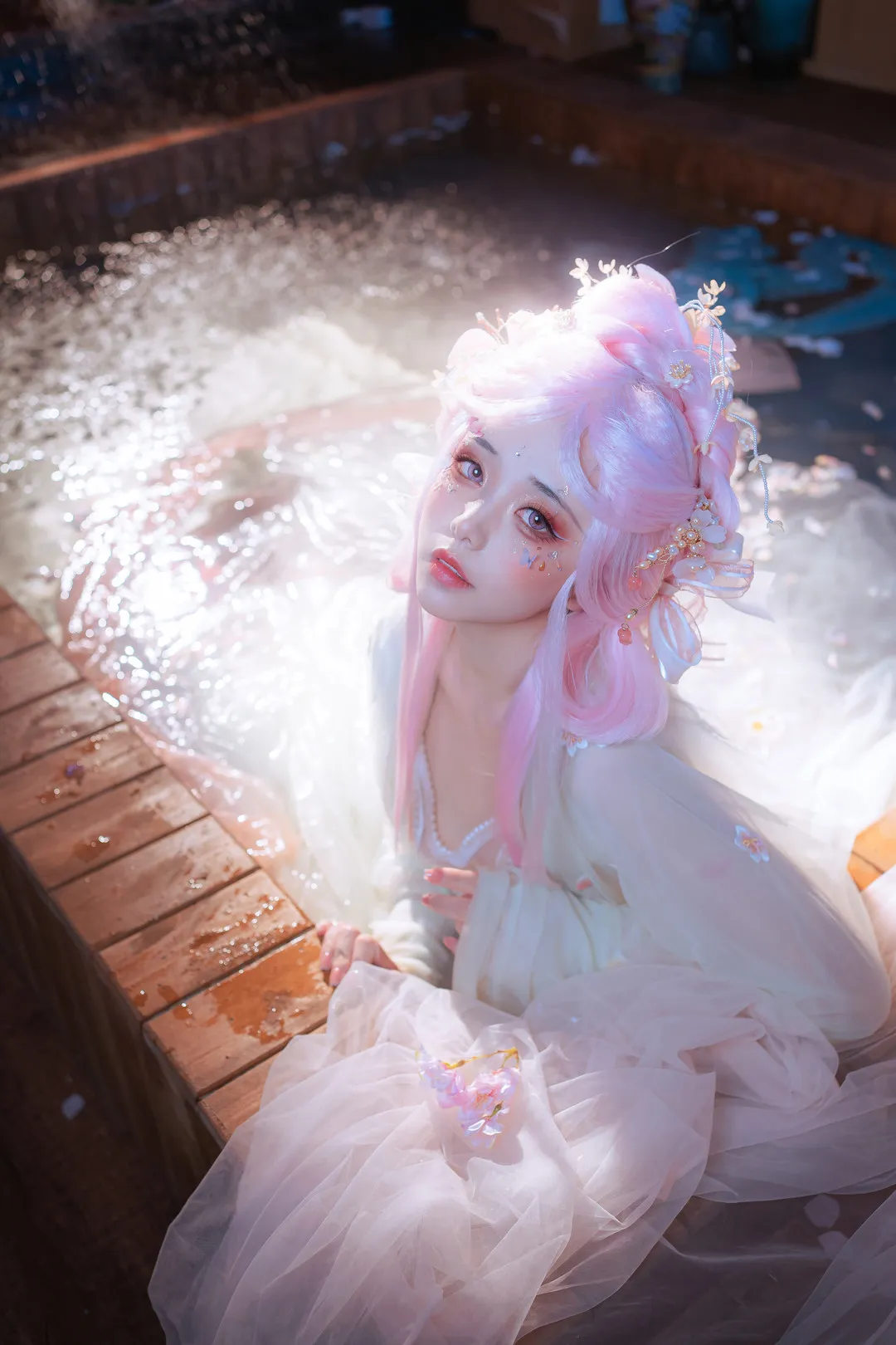 爆机少女喵小吉身着浅色汉服浸于撒满花瓣的木质边缘水池中，佩戴粉色假发与发簪头饰