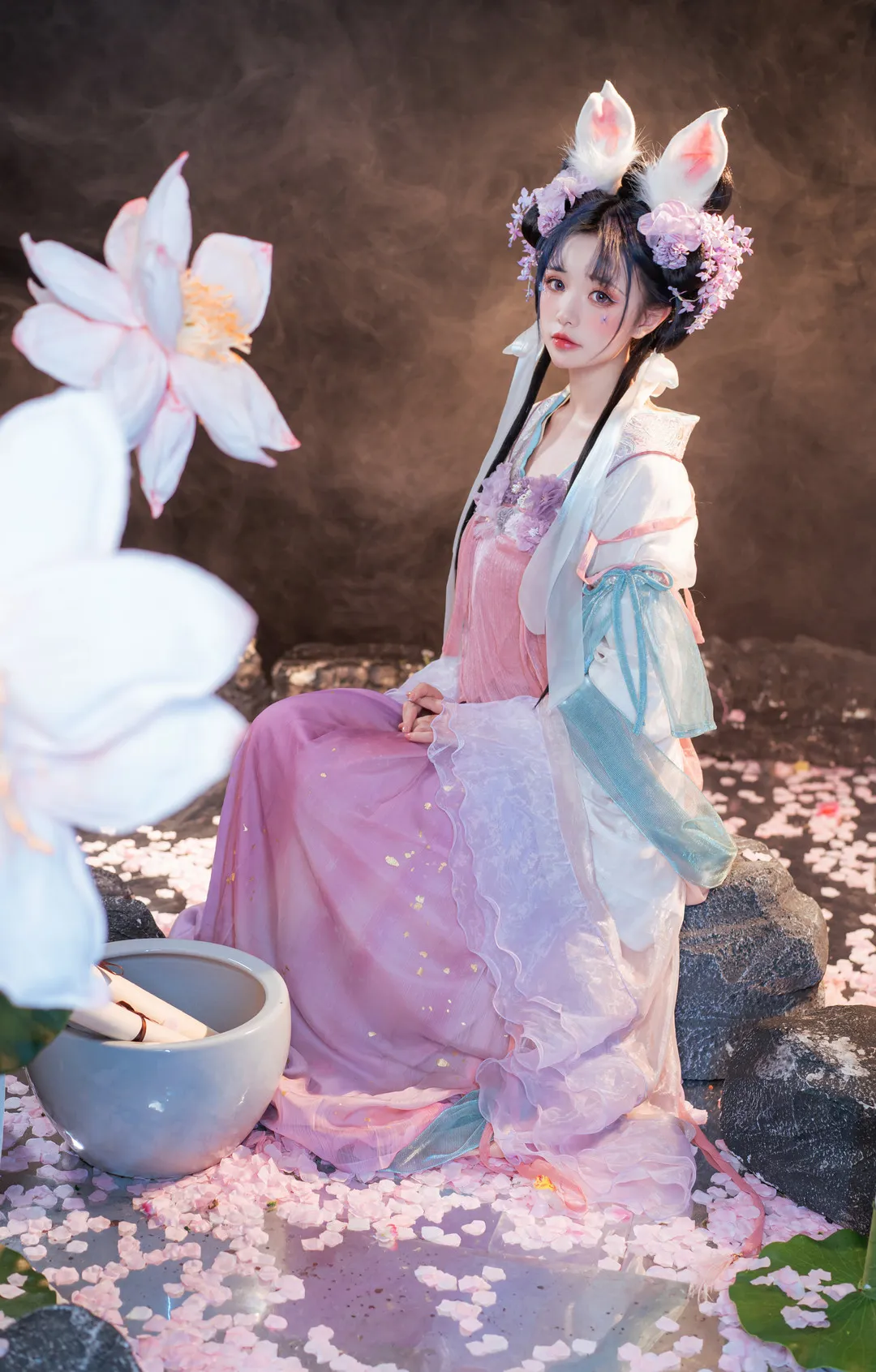 爆机少女喵小吉头戴兔耳发饰身着粉紫色广袖襦裙端坐于室内石块布景上
