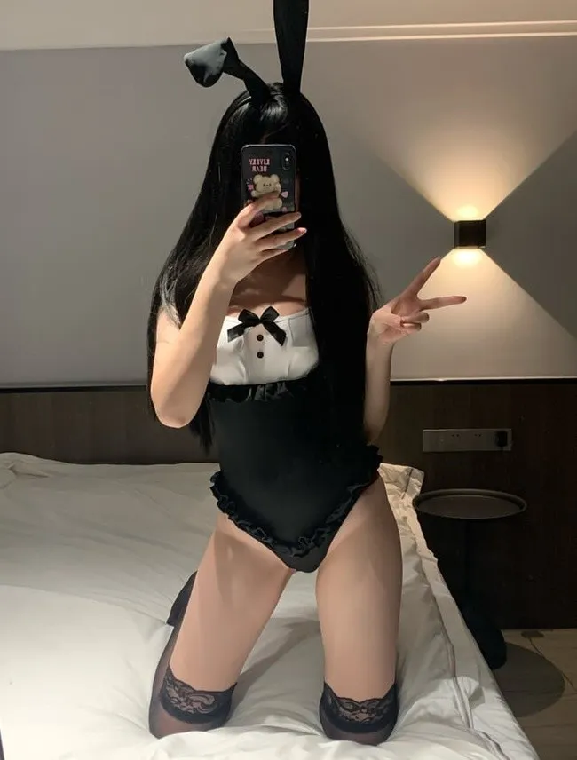 黑色长发佩戴黑色兔耳发箍,身穿黑白拼接低胸连身衣跪在白色床铺上对镜自拍