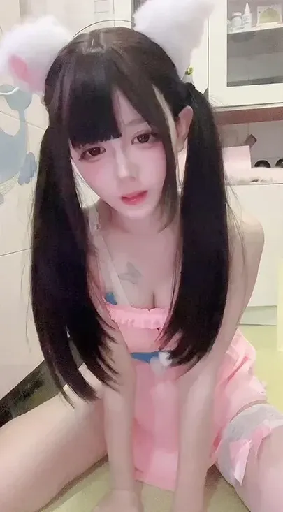 模特头戴白色毛绒猫耳身着粉色吊带居家连衣裙在卫浴间坐姿自拍