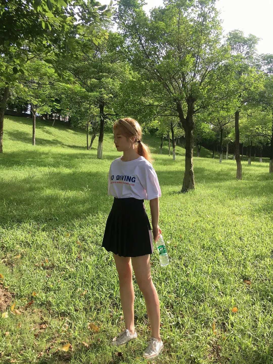 户外林荫绿草坪白色印花短袖T恤配黑色百褶短裙银色运动鞋立姿