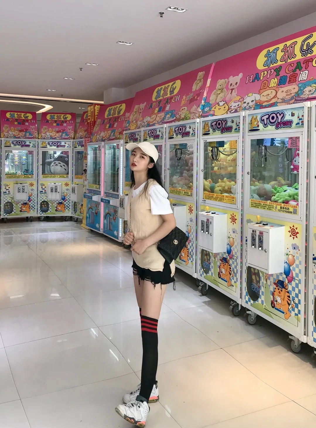 商场电玩娃娃机前米色棒球帽马甲短裤黑色过膝长筒袜老爹鞋立姿抓拍