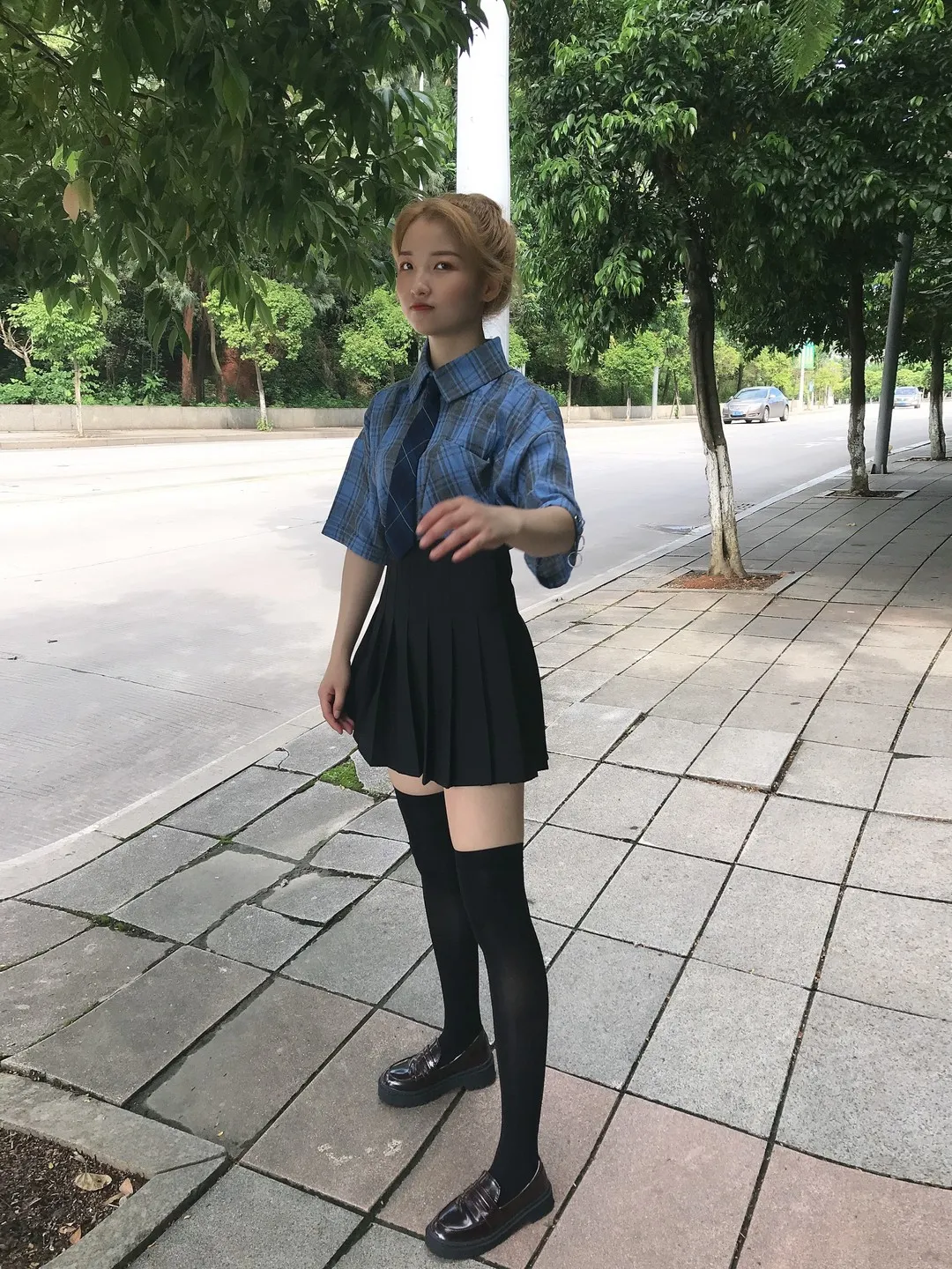 人行道绿荫旁蓝色牛仔短袖衬衫配黑色百褶裙黑色过膝袜侧立抓拍