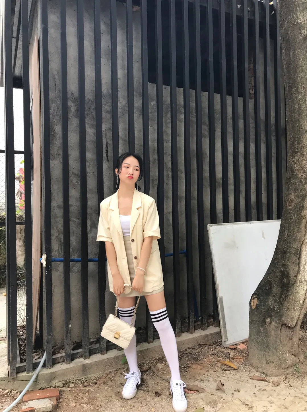 黑色铁栅栏前浅米黄色西装短袖短裤套装条纹过膝袜配纯白运动鞋立姿